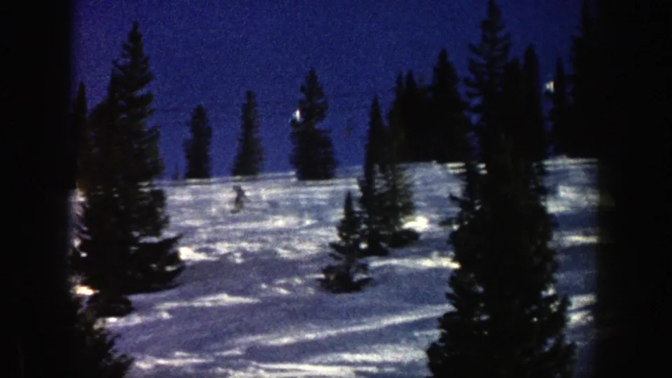 Wide 8mm view of an Aspen ski slope in 1961, with evergreen trees and a small skier moving across the snow.