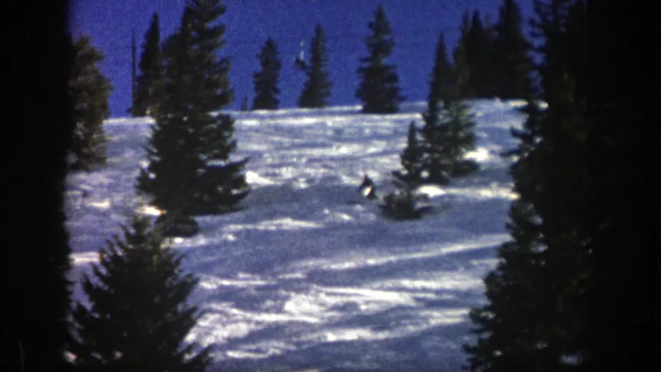 Near the end of the clip, the skier passes toward the right side of the 1961 Aspen snow slope, surrounded by evergreen silhouettes.