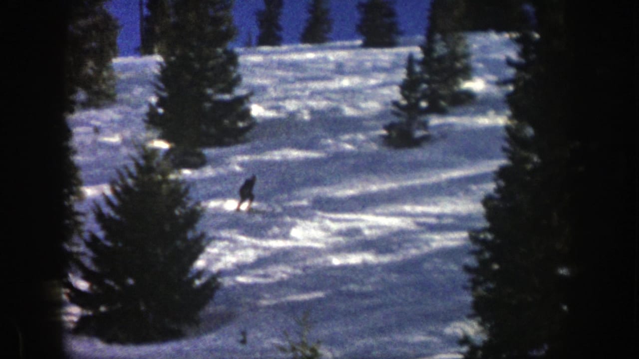 A distant skier descends an Aspen, Colorado snow slope in 1961, framed by dark evergreen trees on 8mm home-movie film.