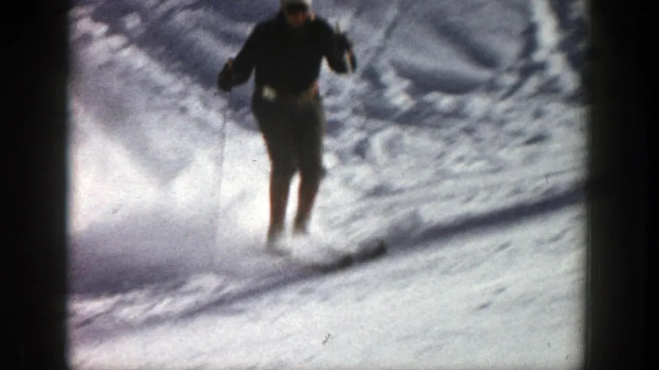 The skier comes closer to the camera on the bright Aspen slope, partially softened by motion, grain, and snow spray.