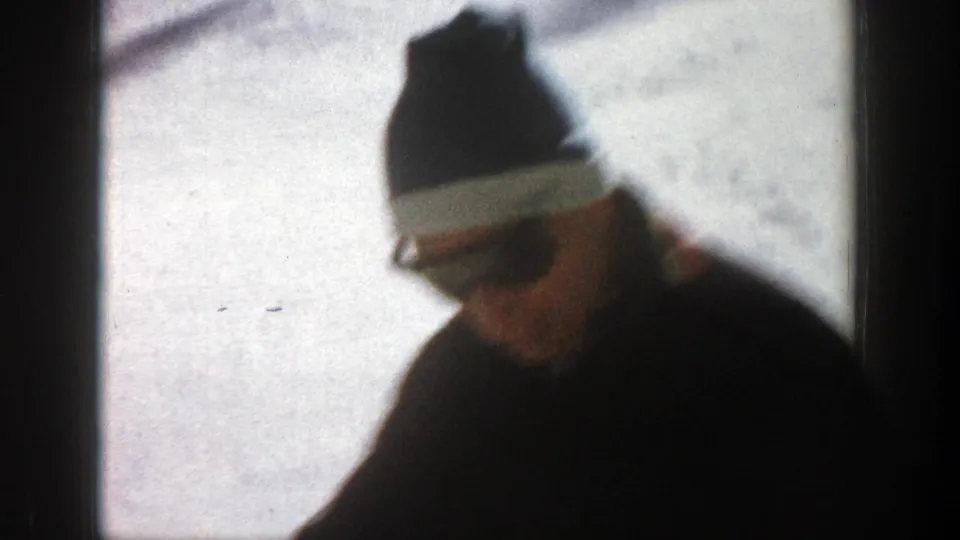 A bundled adult man in a knit cap stands in a snowy Aspen, Colorado landscape in 1961 home-movie footage.
