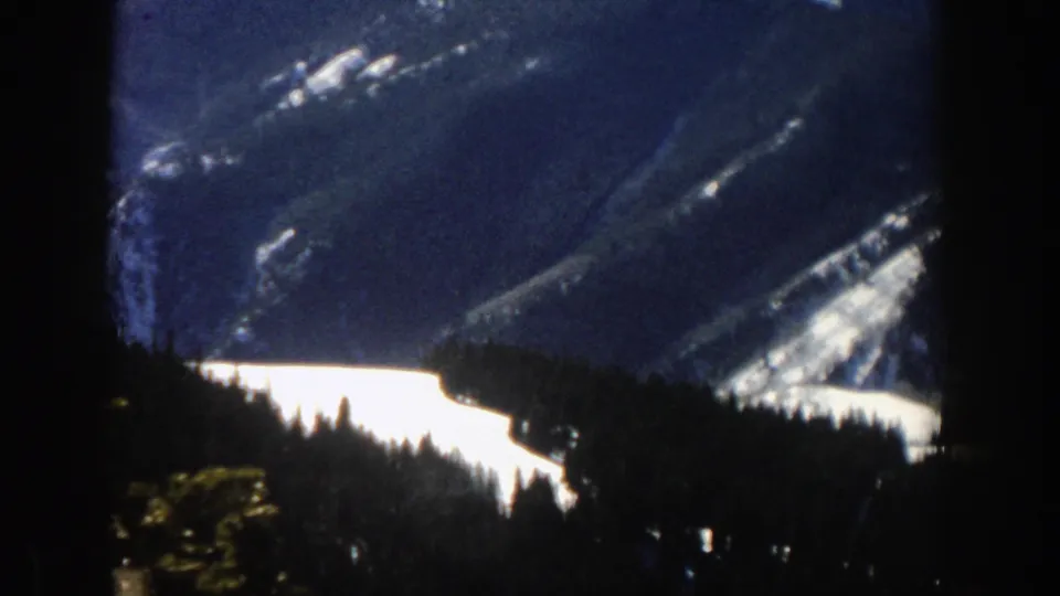 A dark evergreen foreground overlooks a snowy alpine valley and distant mountain slopes near Aspen, Colorado.