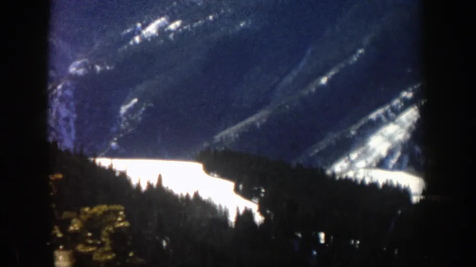 1961 Aspen-area mountain view with snowfields, evergreen trees, and dark window framing in grainy 8mm footage.