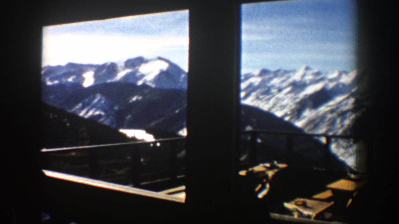 Snowy mountain range seen through dark window frames from a balcony area.