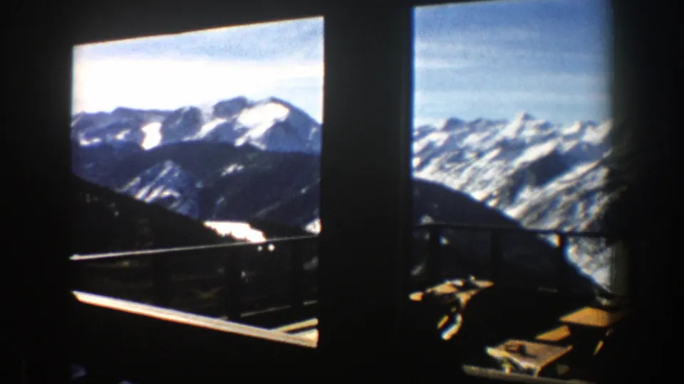 1961 Aspen home-movie frame showing snow-capped mountains through dark window openings with balcony railing below.
