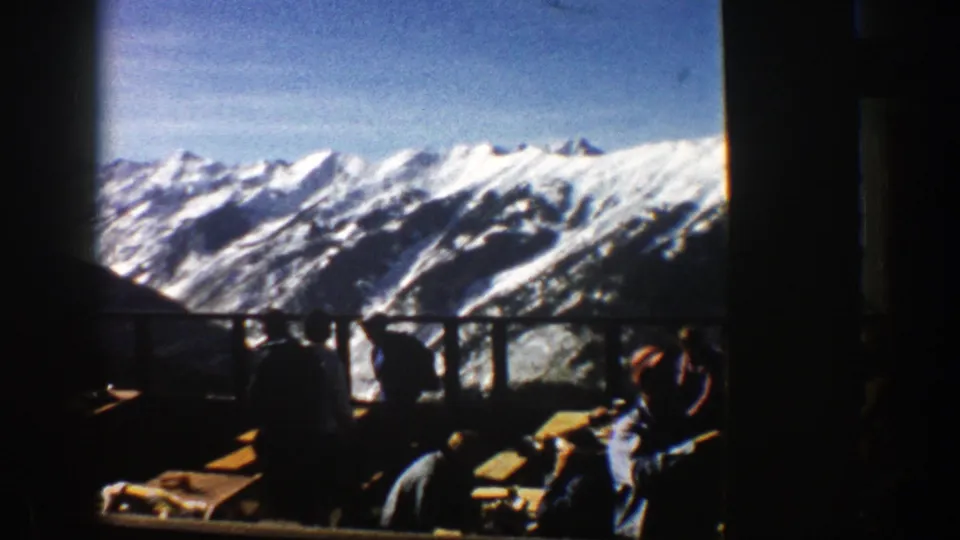 Aspen, Colorado resort balcony scene with guests in shadow and a bright alpine panorama beyond the railing.