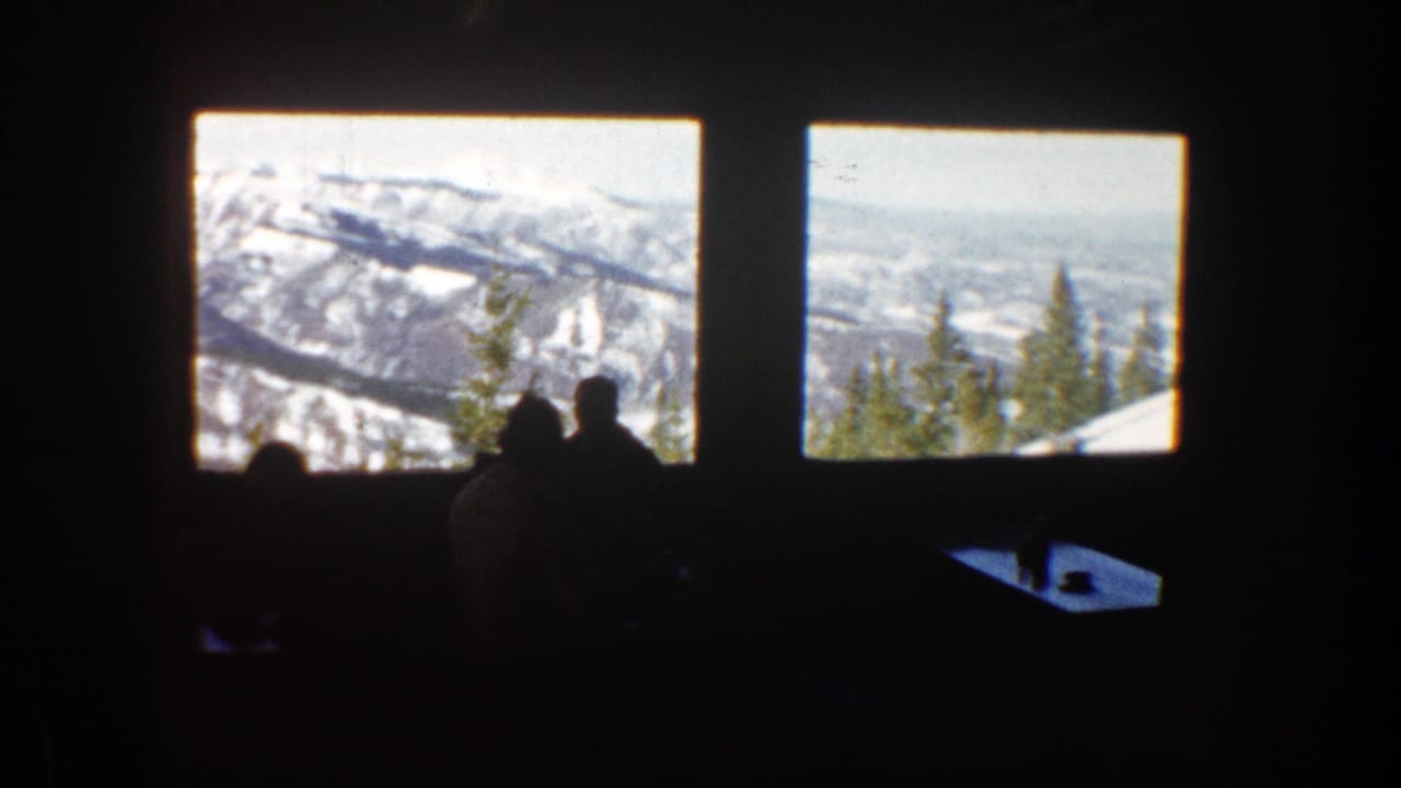 Silhouetted people sit in a dark room facing two bright windows with snowy mountains outside.