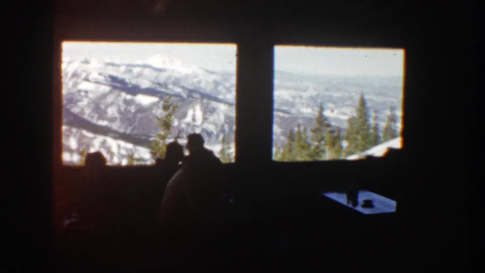 Aspen, Colorado 1961 frame with silhouetted people in a dark room watching snowy mountains through two large windows.
