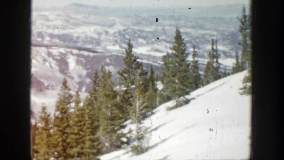 1961 Aspen, Colorado 8mm frame with foreground evergreens, snowfields, and distant ridges softened by film grain.