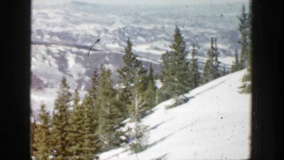 1961 Aspen, Colorado winter landscape with evergreen trees, a sloping snowfield, distant ridges, and visible 8mm film wear.