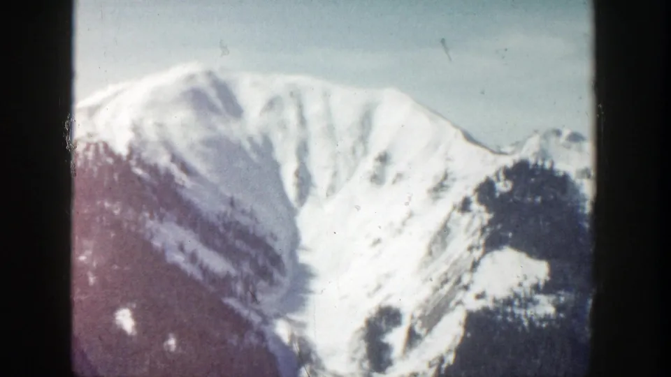 Vintage 8mm frame from Aspen, Colorado showing a snow-covered alpine slope and blue sky with visible film softness.