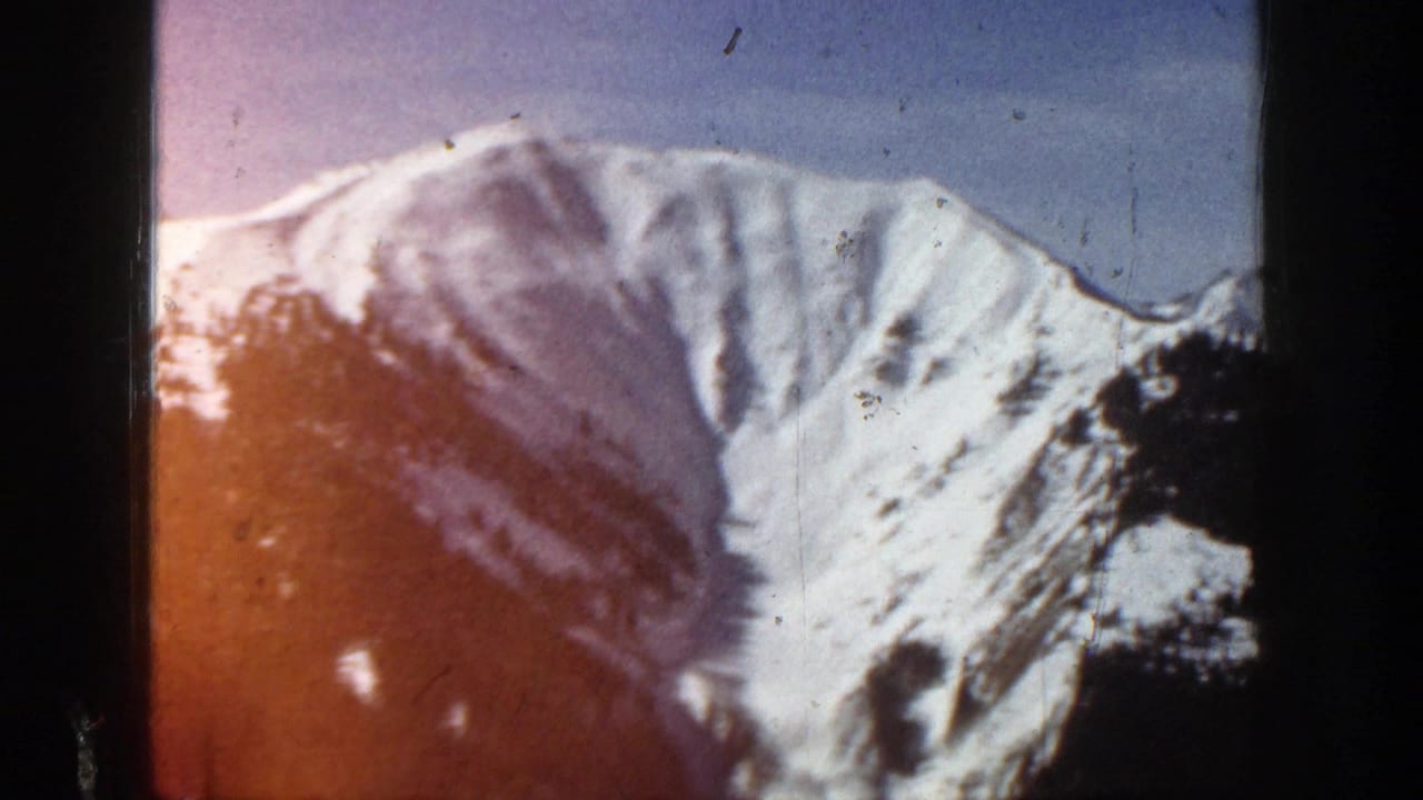 Aspen, Colorado 1961 home-movie frame showing a snowy mountain ridge with soft focus, film grain, and dark frame edges.