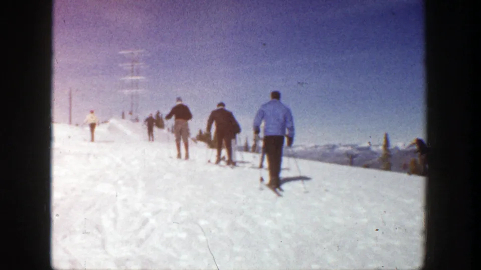 Aspen, Colorado 1961 frame showing a rear-view group of skiers climbing a bright slope, with a blue-coated skier closest to camera.