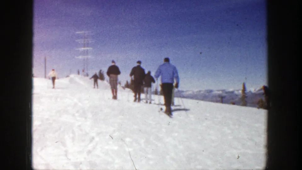 1961 Aspen 8mm frame of skiers moving uphill across a snow-covered slope, with distant mountain views and visible film grain.