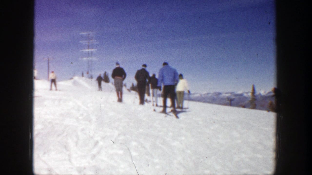 Skiers walk up a snowy hill under a blue sky.
