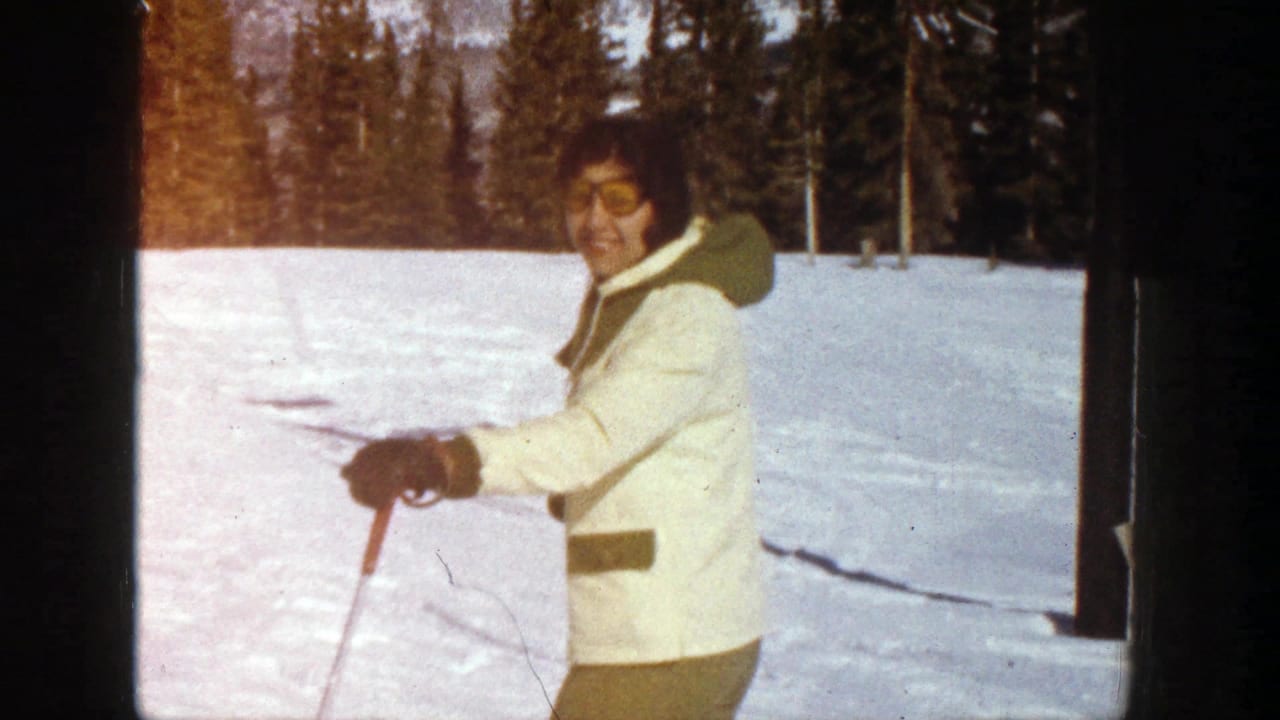 Smiling skier in a cream jacket holds ski poles on snow.