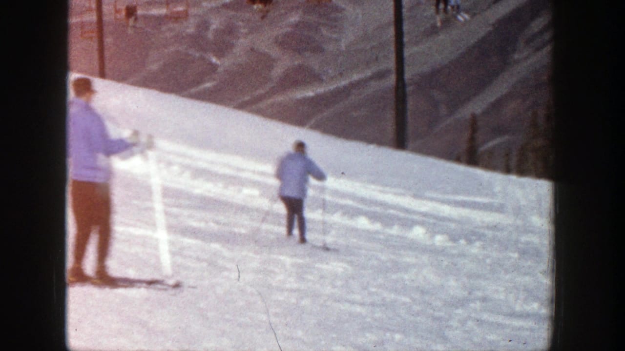 Two skiers on a sunlit snowy slope with mountains in the background.