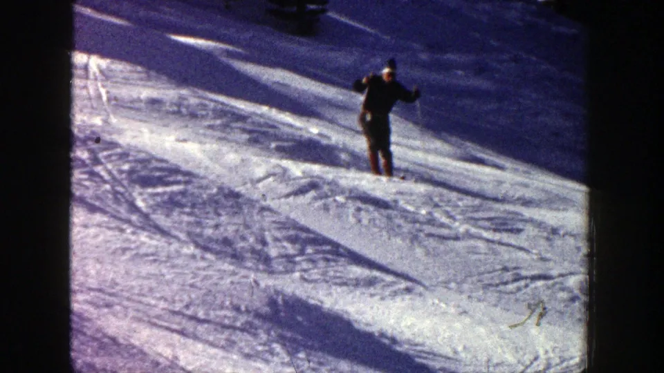 1961 Aspen home-movie frame showing a skier in dark clothing on a textured snow slope with strong shadows.