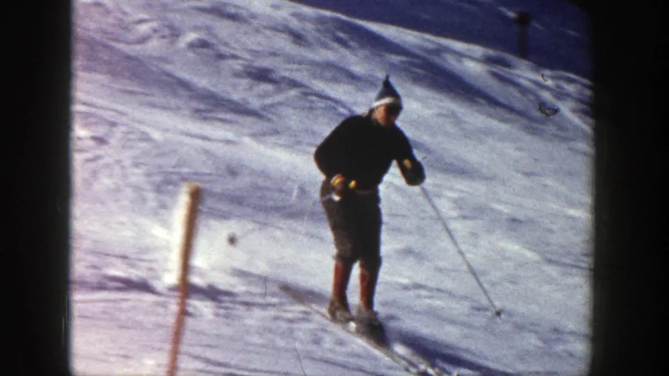In the Aspen 1961 home-movie frame, an adult skier passes a marker post while descending a snowy mountain slope.