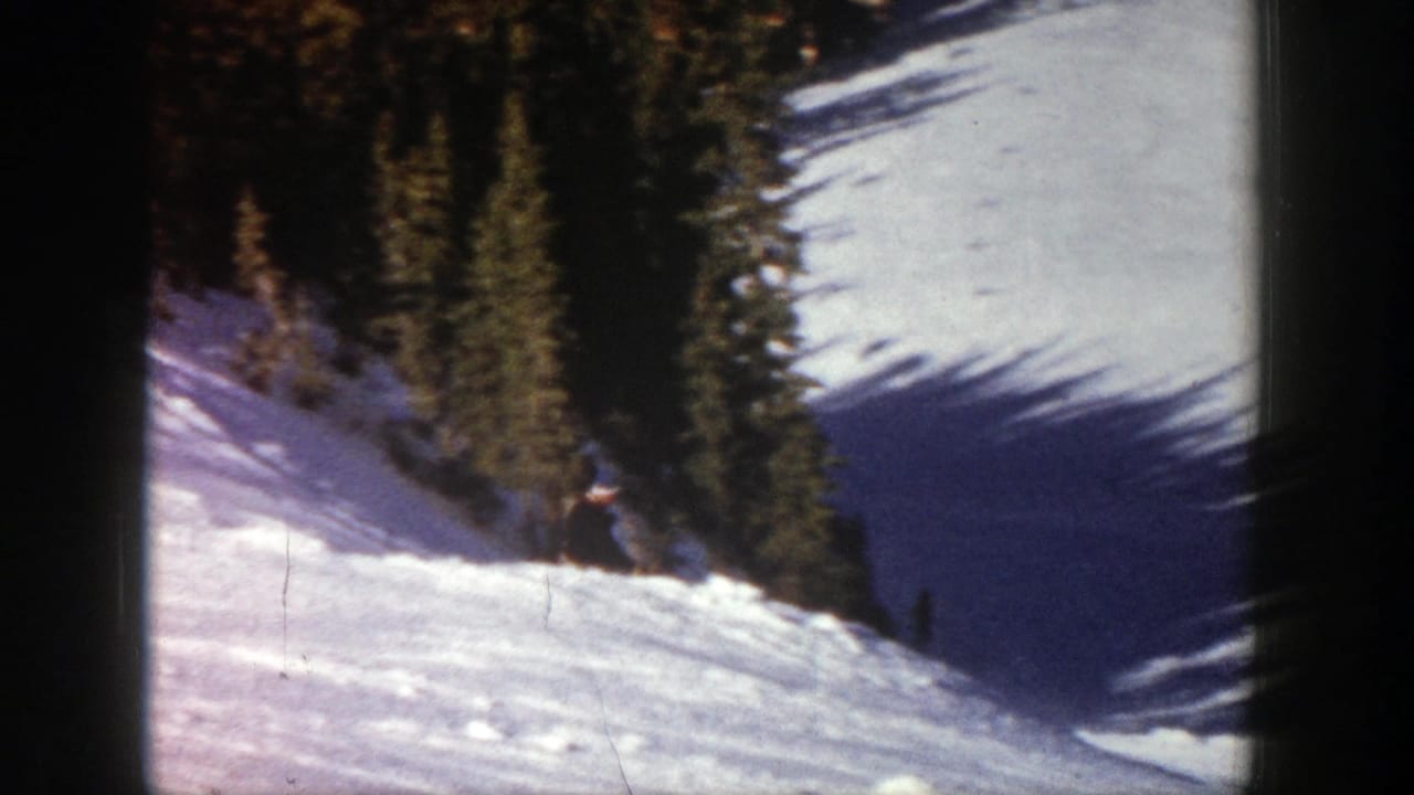 A distant skier in dark clothing descends a snowy Aspen slope in 1961, with evergreen trees along the run.