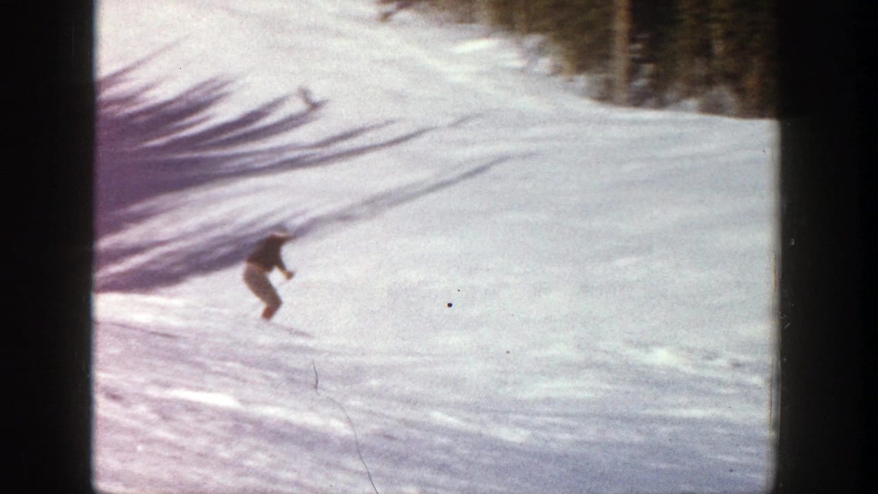Skier descending across open snow with long shadows behind.