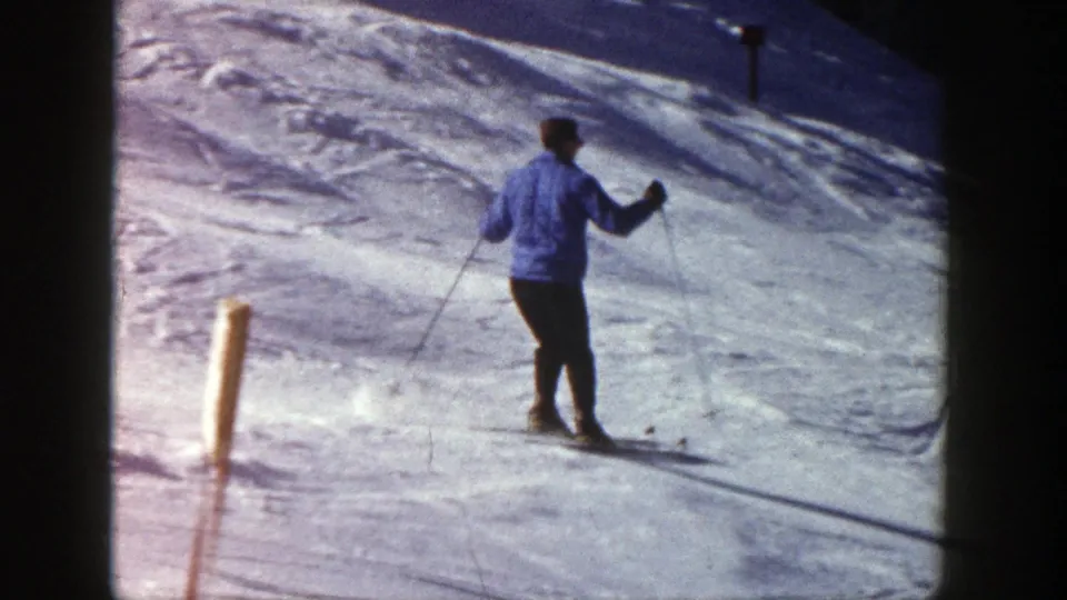 A rear view shows the skier gliding near a simple slope marker, with textured snow and shadows in the frame.