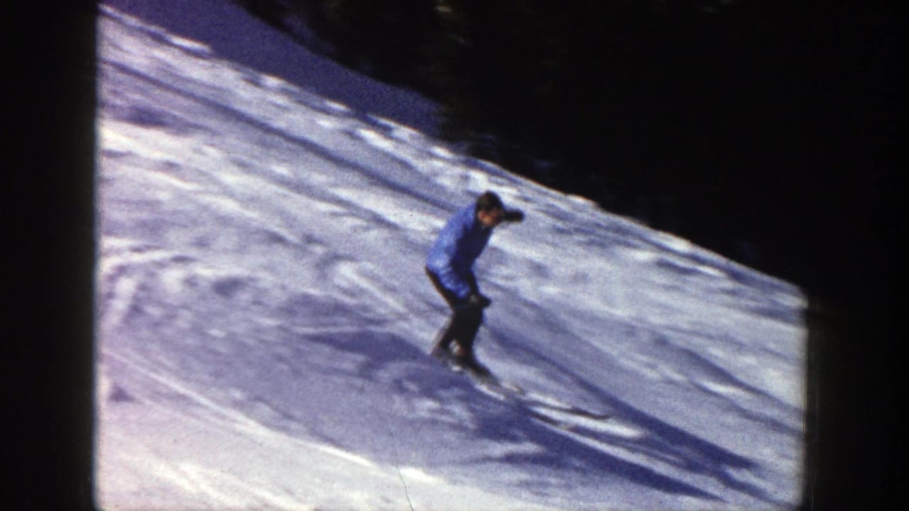 Man in a blue jacket skis down a snowy slope near dark evergreen trees.
