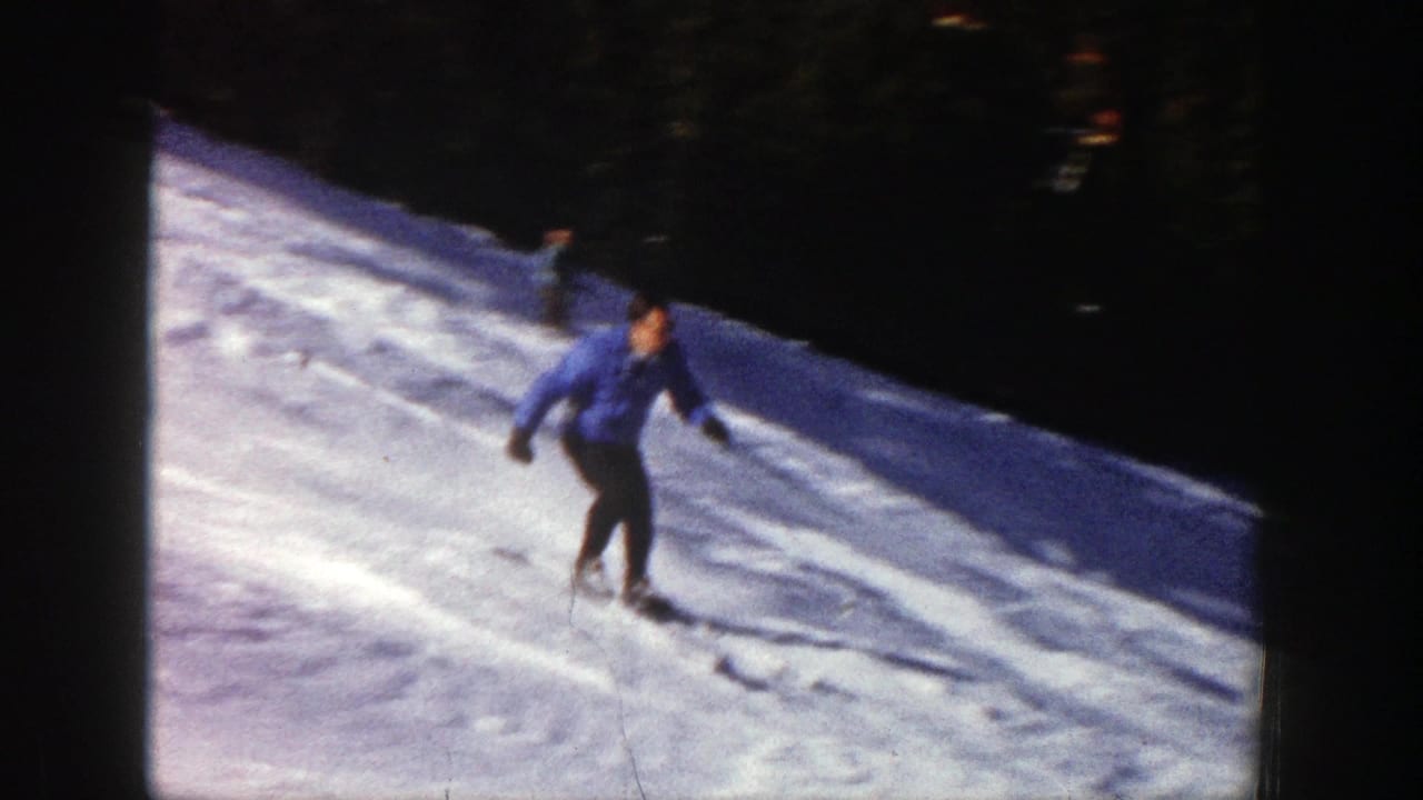 Skier in blue turns across a snow slope with trees behind him.