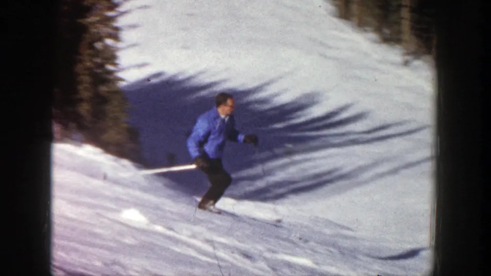Near the end of the clip, the skier descends through long shadows on a snow trail lined with evergreens.