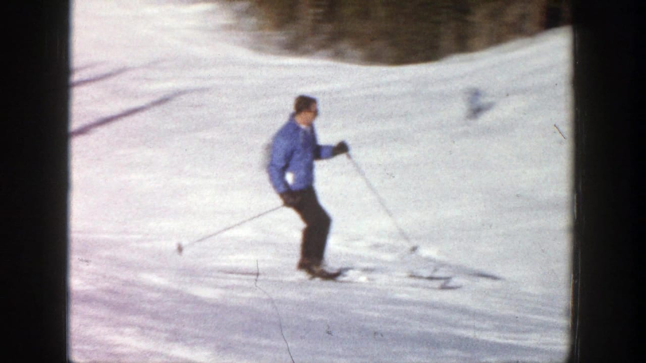 Adult man in a blue sweater and dark pants skis on a sunlit Aspen snow slope in 1961 home-movie footage.