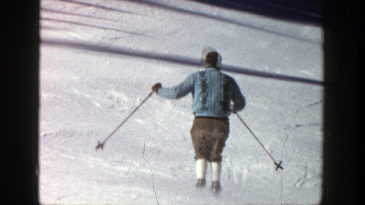 A skier in Aspen, Colorado, 1961, seen from behind in a light sweater and brown pants while starting down a snowy slope.