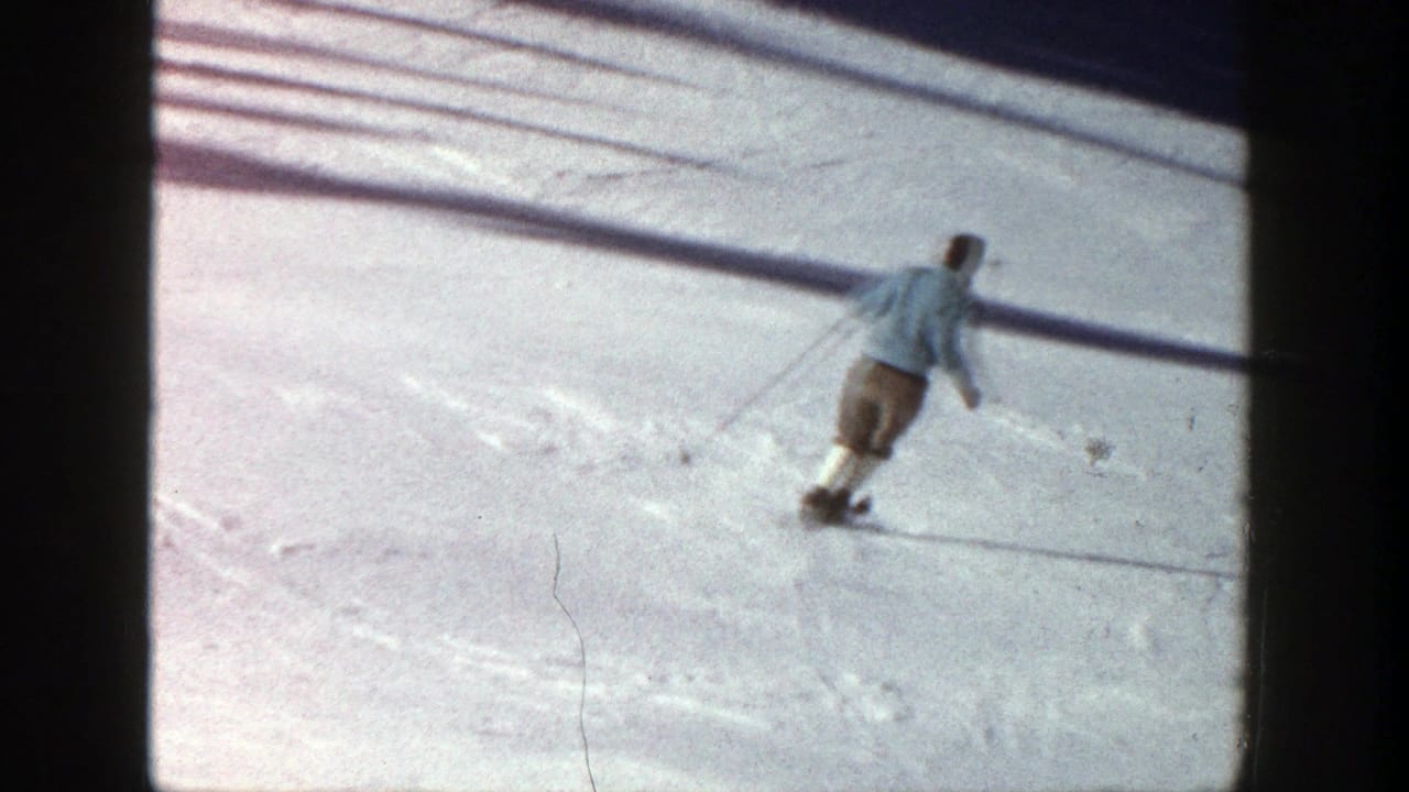 Skier turns across bright snow with poles trailing behind.