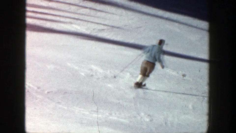 The skier carves across the Aspen snowfield, with long poles and narrow skis visible in the 1961 home-movie frame.