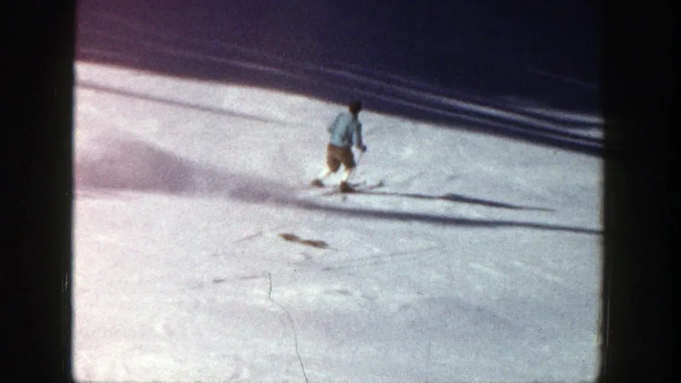 A distant skier continues downhill on the Aspen slope, framed by snow texture and dark 8mm border edges.