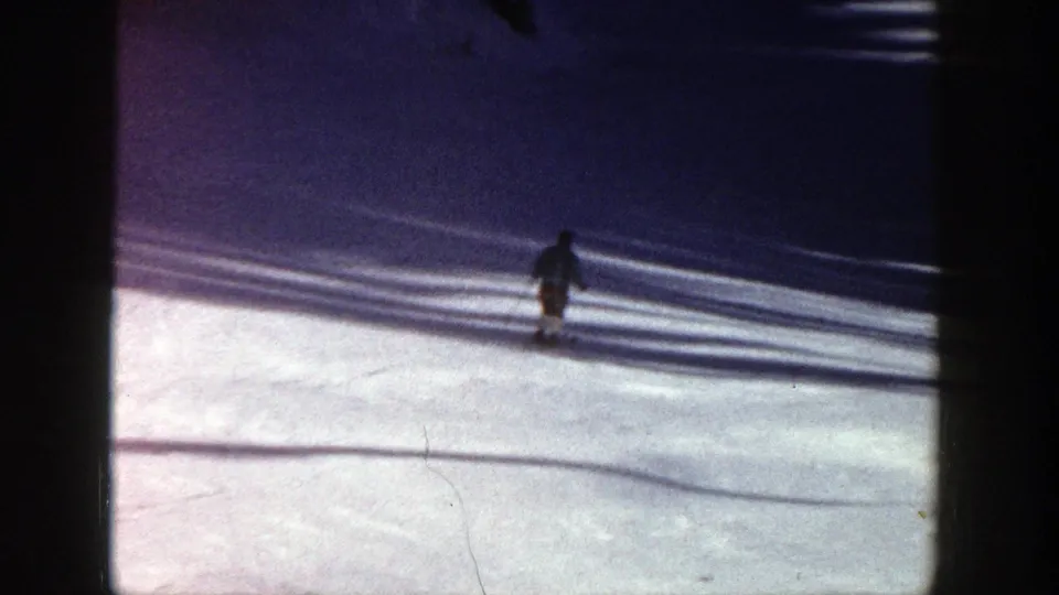 The skier is small in frame near broad shadows on an Aspen snow slope, ending the short 1961 8mm skiing view.