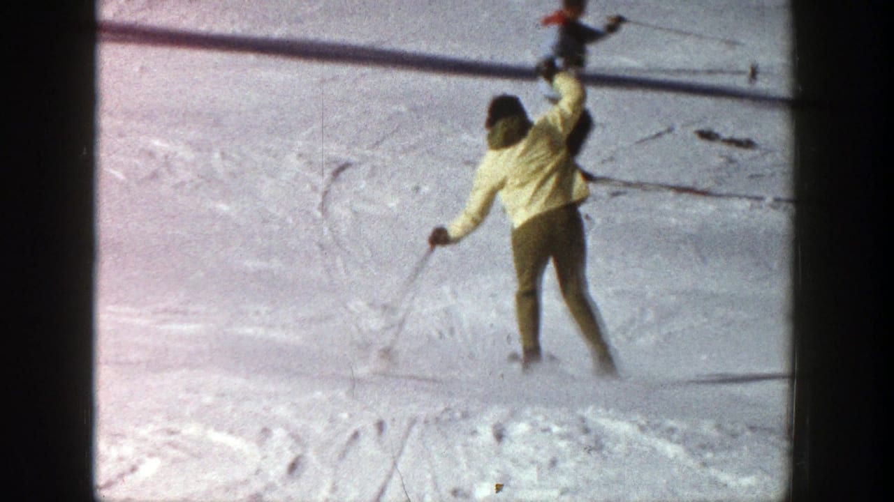 Skier in a yellow jacket raises one arm while descending a snowy slope.