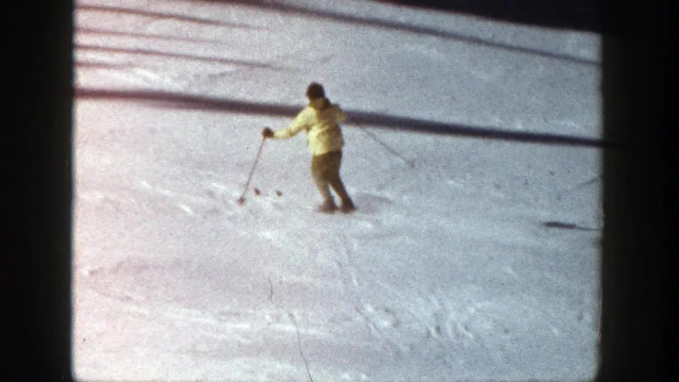 1961 Aspen home-movie still of a skier in a yellow jacket carving gently across a marked snowy slope.