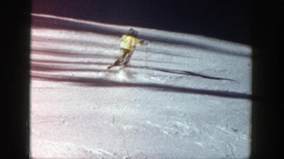 Wide 1961 Aspen frame showing the skier farther down the snowy hill, with long shadows crossing the slope.