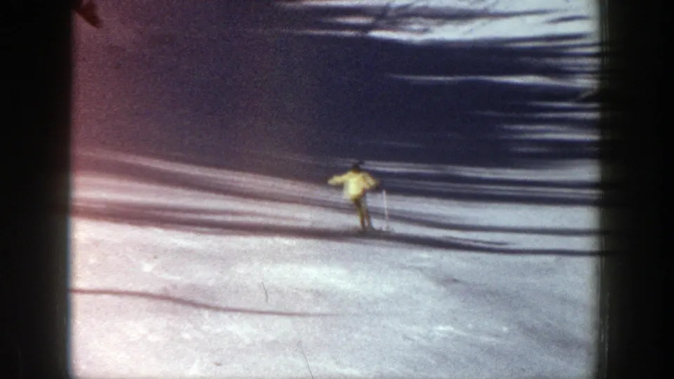 Near the end of the 1961 Aspen clip, the skier in yellow descends across bright snow crossed by dark horizontal shadows.