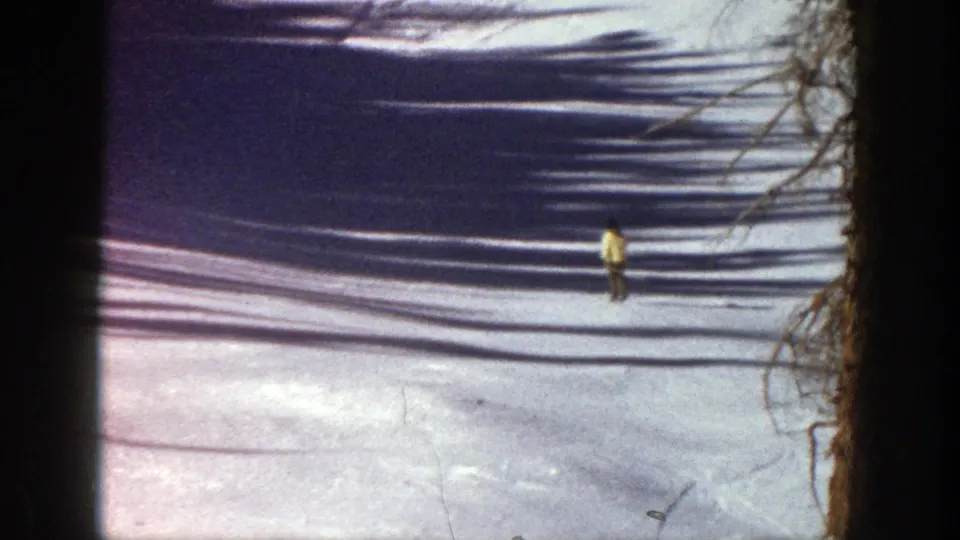 1961 Aspen ski footage frame with the skier farther down the snowfield, framed by dark film borders and tree shadows.