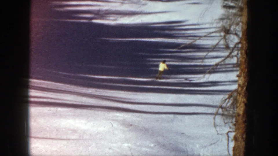 Aspen, Colorado 1961 frame showing a lone skier crossing a tree-lined snowy run in grainy 8mm color.