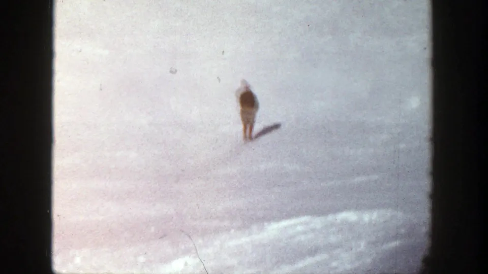 A distant skier appears near the center of a broad snowy Aspen slope, reduced to a small figure within the winter landscape.