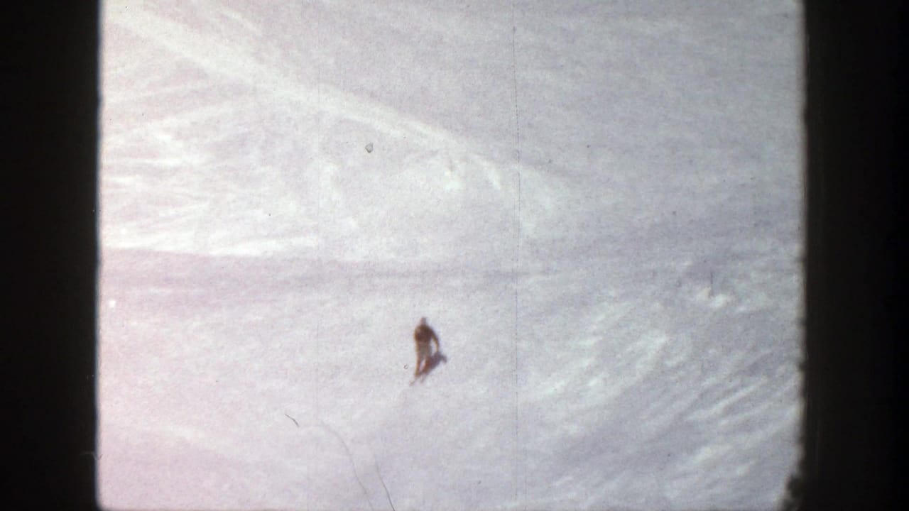 Distant skier in a dark jacket crossing a bright snowy slope.