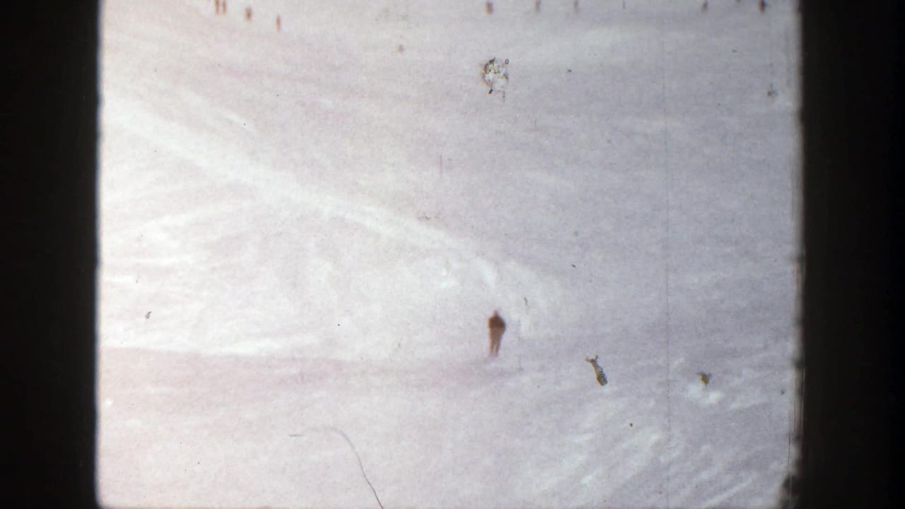 Small skier figure on a pale snowy slope with film scratches visible.