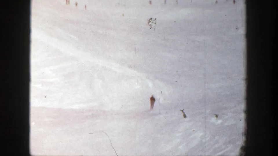 A small skier descends a wide Aspen snowfield, with faded color and scratches from the 8mm source visible.