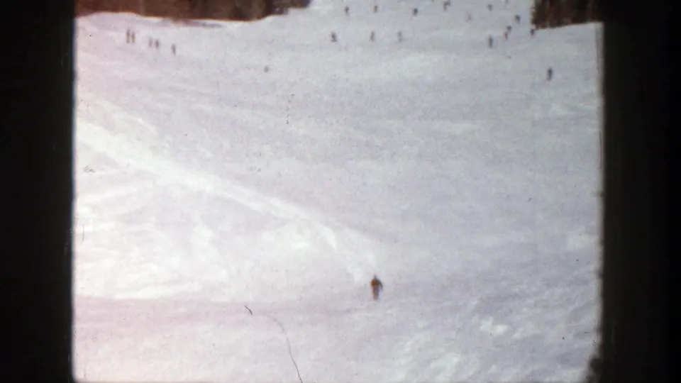 Wide 1961 Aspen ski slope view with one nearer skier and scattered distant figures near a dark tree line.