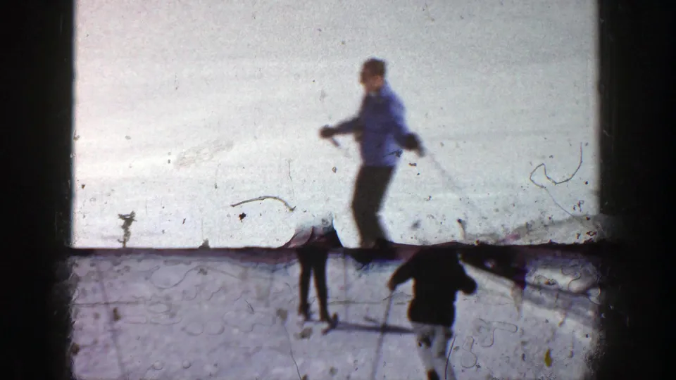 A soft 8mm frame shows a skier crossing the foreground while other skiers continue downhill on the snowy Aspen slope.
