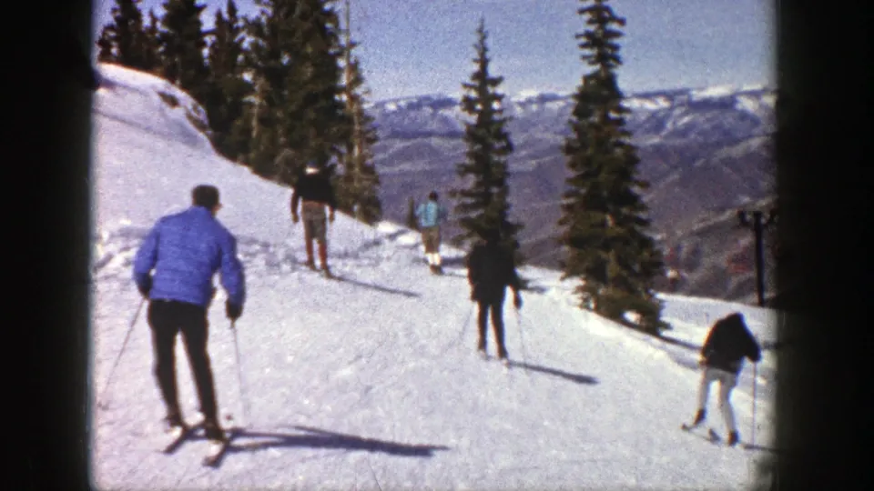 Aspen, Colorado ski-practice frame from 1961 with a blue-jacketed skier moving behind others on a sunny trail.