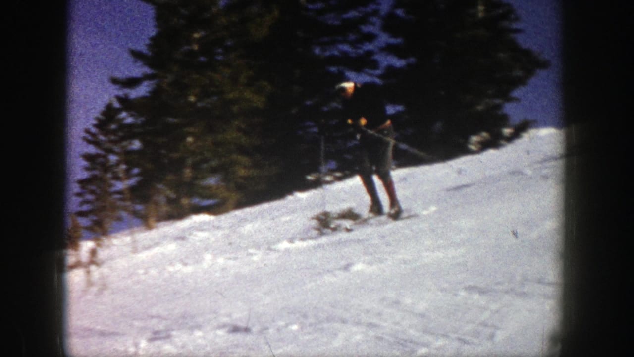 A skier in Aspen, Colorado, 1961, moves across a snowy slope near evergreens in a grainy 8mm frame.