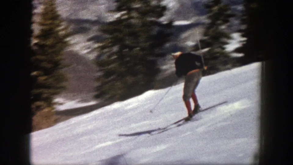 A rear view of the skier on an Aspen slope, with evergreens and distant snowy terrain visible in the 8mm frame.